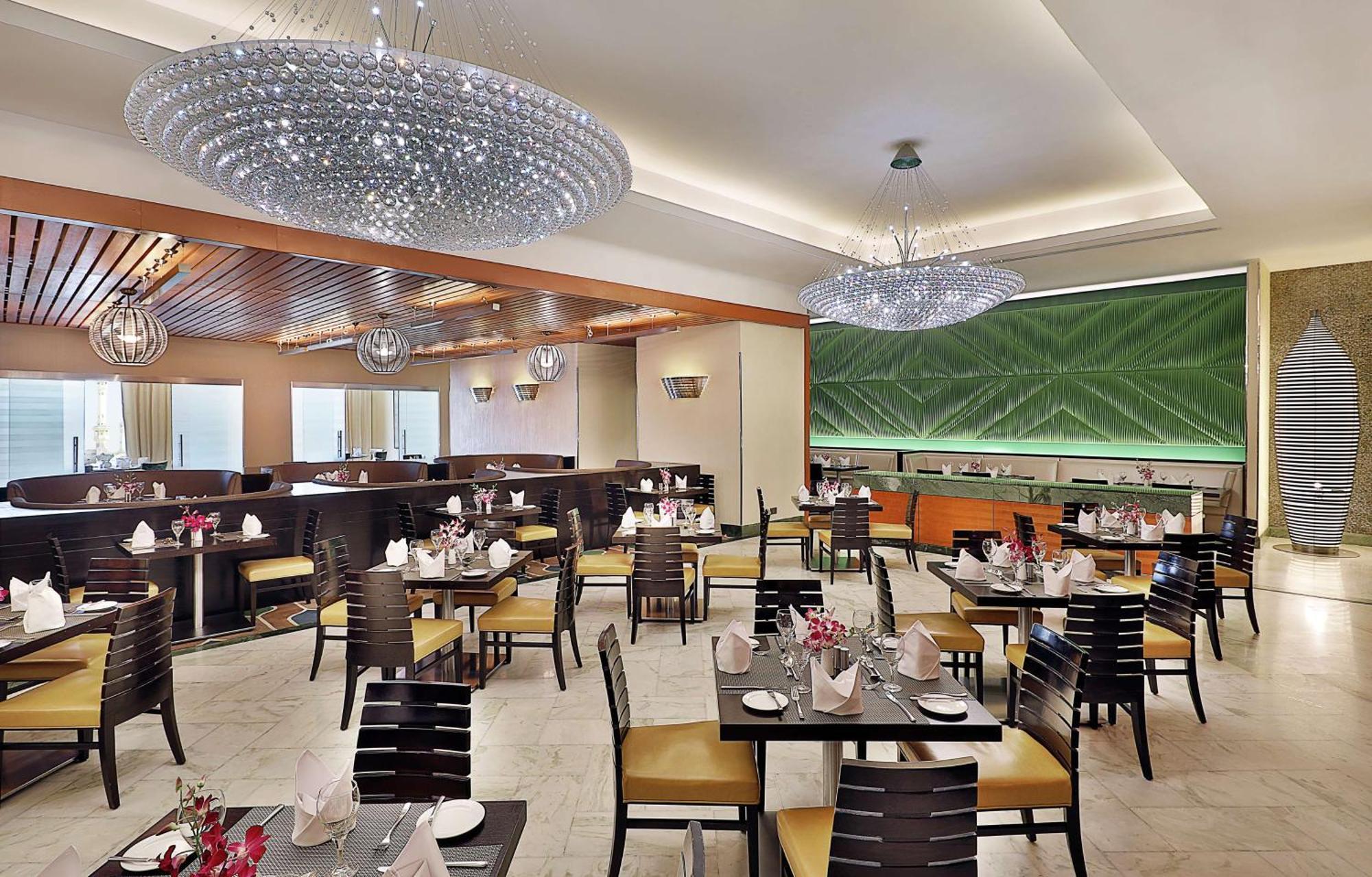希尔顿套房麦加酒店 Mecca 外观 照片 The photo features an elegant restaurant interior. It has a modern design with light-colored walls and wooden accents. The space is furnished with dark wooden tables and chairs, each set with neatly arranged tableware, including napkins and small cen